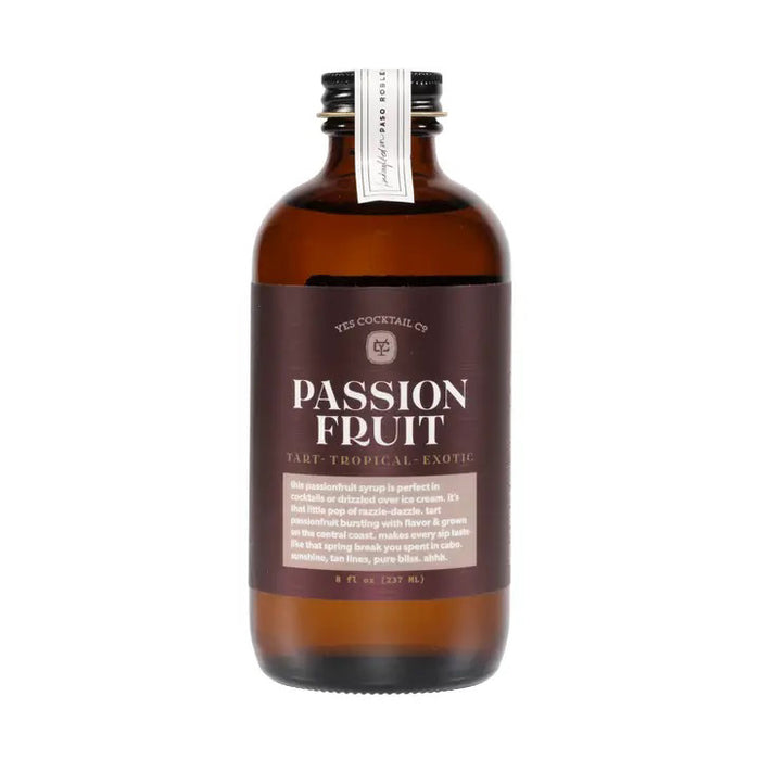 YES COCKTAIL CO. Passionsfruit Syrup comes in a brown glass bottle with a black cap and white neck tag, offering tart, tropical flavors ideal as a dessert topping or as a delicious mixer for tropical cocktails.
